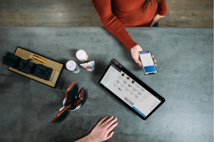 In The Signal fintech roundup, a person scans a smartphone beside a tablet, beauty items and a tray while tokenized deposits are discussed.