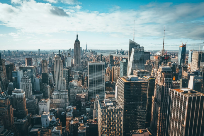 Manhattan skyline stretches under a bright blue sky, with the Empire State Building rising above dense towers in New York City.